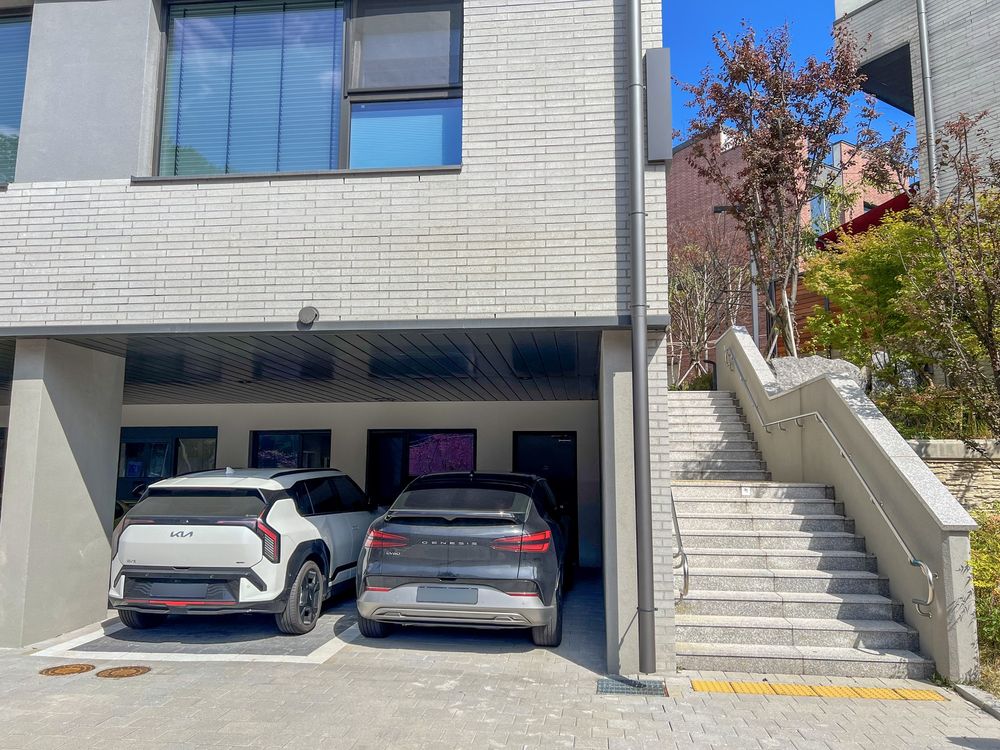 집 앞 지붕 아래 주차 공간에 세운 차 2대와 옆 계단